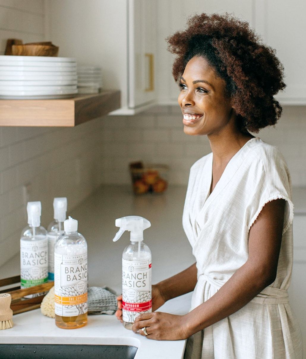 Woman standing in kitchen with a Branch Basics bottle